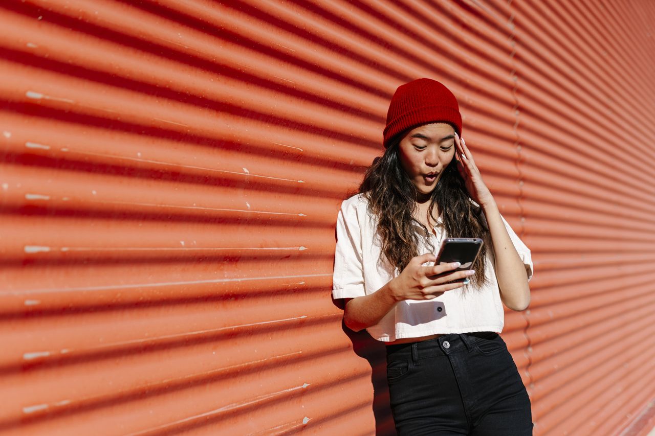 Surprised woman using mobile phone in front of corrugated wall