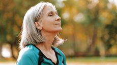 An older woman looks calm, her head back and eyes closed while she stands outside.