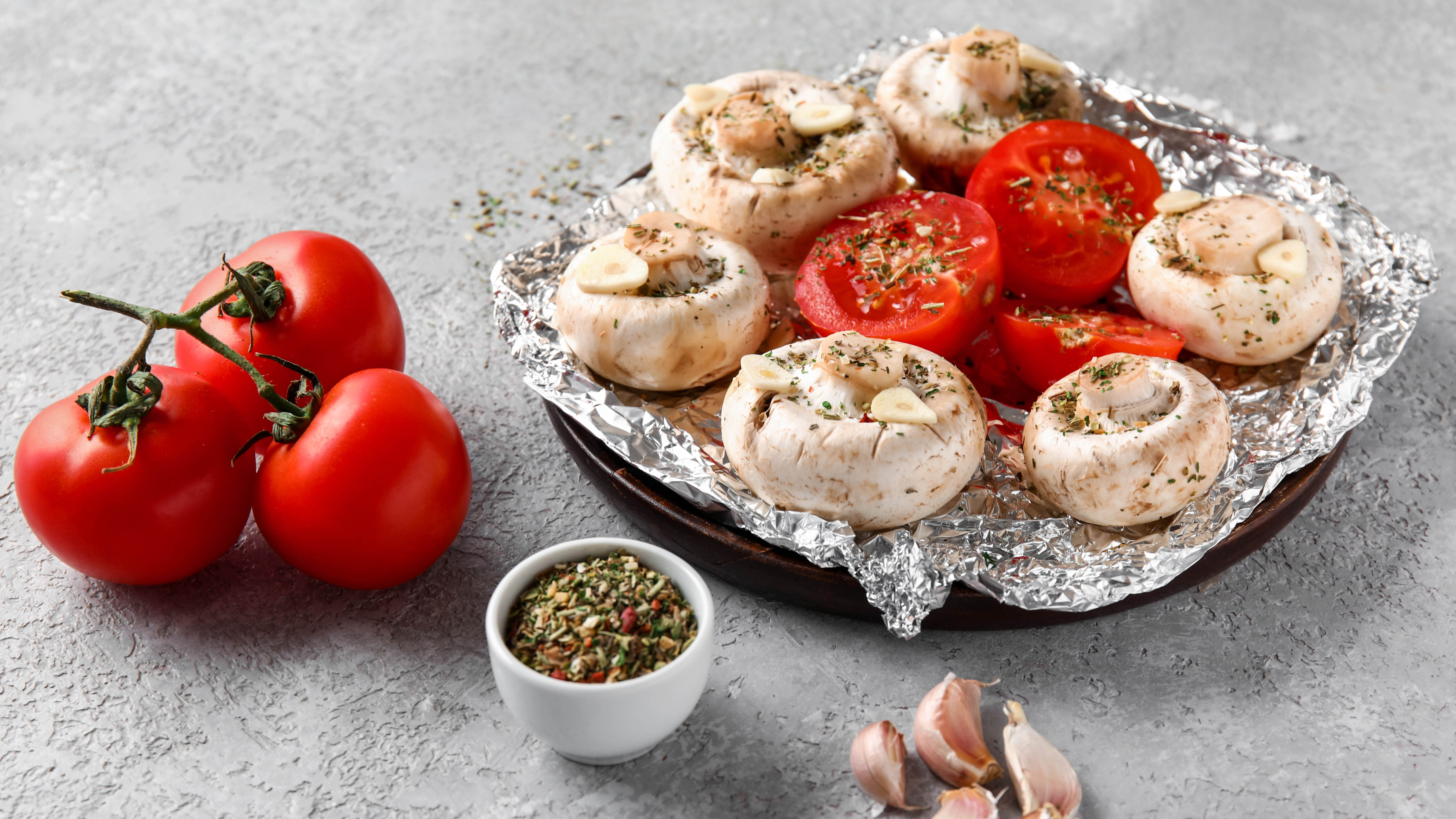 Mushrooms and tomatoes prepared for cooking and placed on aluminium foil