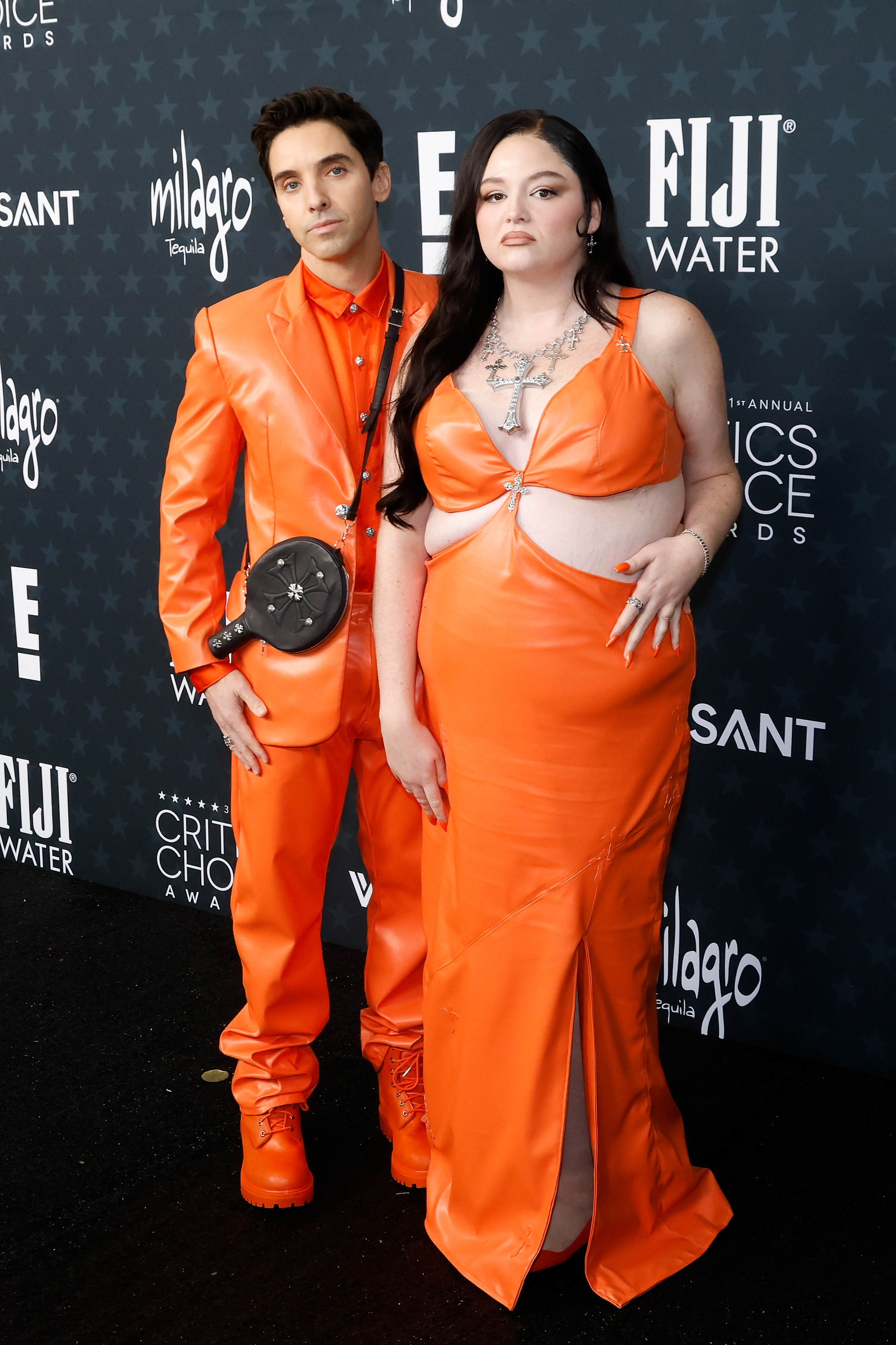 Meg Stalter poses at the 2026 Critics' Choice Awards red carpet in an orange dress