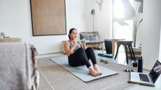 Woman holding a dumbbell on a yoga mat in living room.