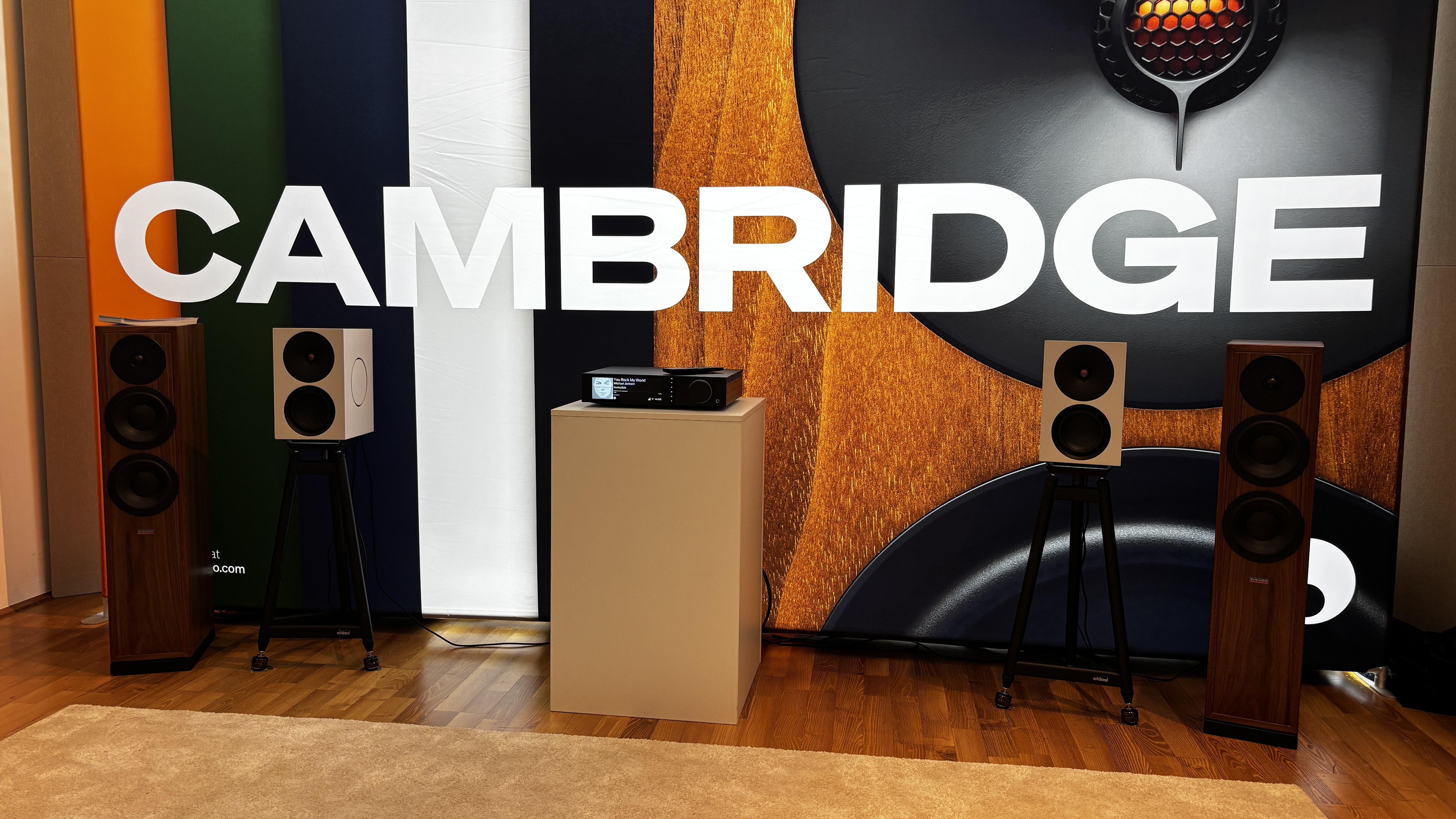Cambridge Audio Evo 300 in the middle of a room flanked by two pairs of speakers. A bright white Cambridge logo is in the background