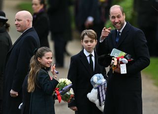 Prince William pointing and smiling at the camera standing with Prince George and Princess Charlotte outside the church on Christmas Day 2024