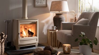 A white log burner in a neutral living room besides a white arm chair and oversized lamp