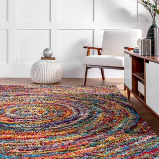 A mult-colored shag rug features a swirl pattern and sits next to white furniture