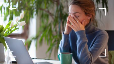 Tired woman leaning over laptop in the daytime with hands over face, asking can menopause cause insomnia