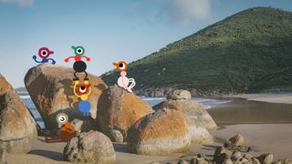 A group of Big Walk characters explore a pile of rocks on a beach