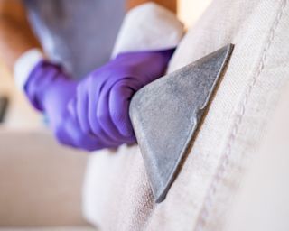 hands in purple rubber gloves vacuuming a couch or sofa - GettyImages-1320317205