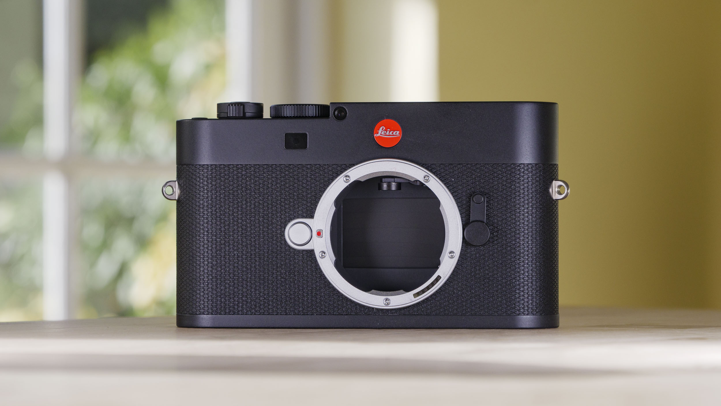 Leica M EV1 camera on a wooden table with glass-panelled door backdrop, no lens attached