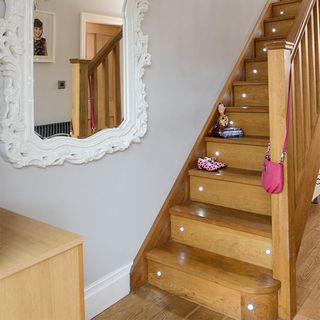 A wooden staircase with built-in stair lights and a white mirror on the wall