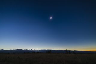 the sky appears dark blue during an eclipse over a distant mountain range