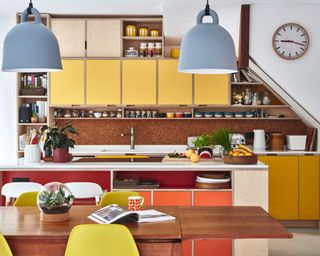 A retro-style kitchen with yellow cabinets, cork backsplash, light blue bell shaped light fixtures, wooden table and yellow chairs