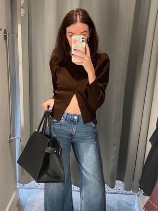 Woman wears brown cardigan, blue jeans, black bag