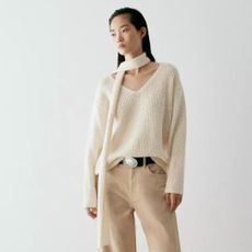 Woman wears cream coat with high collar, black trousers