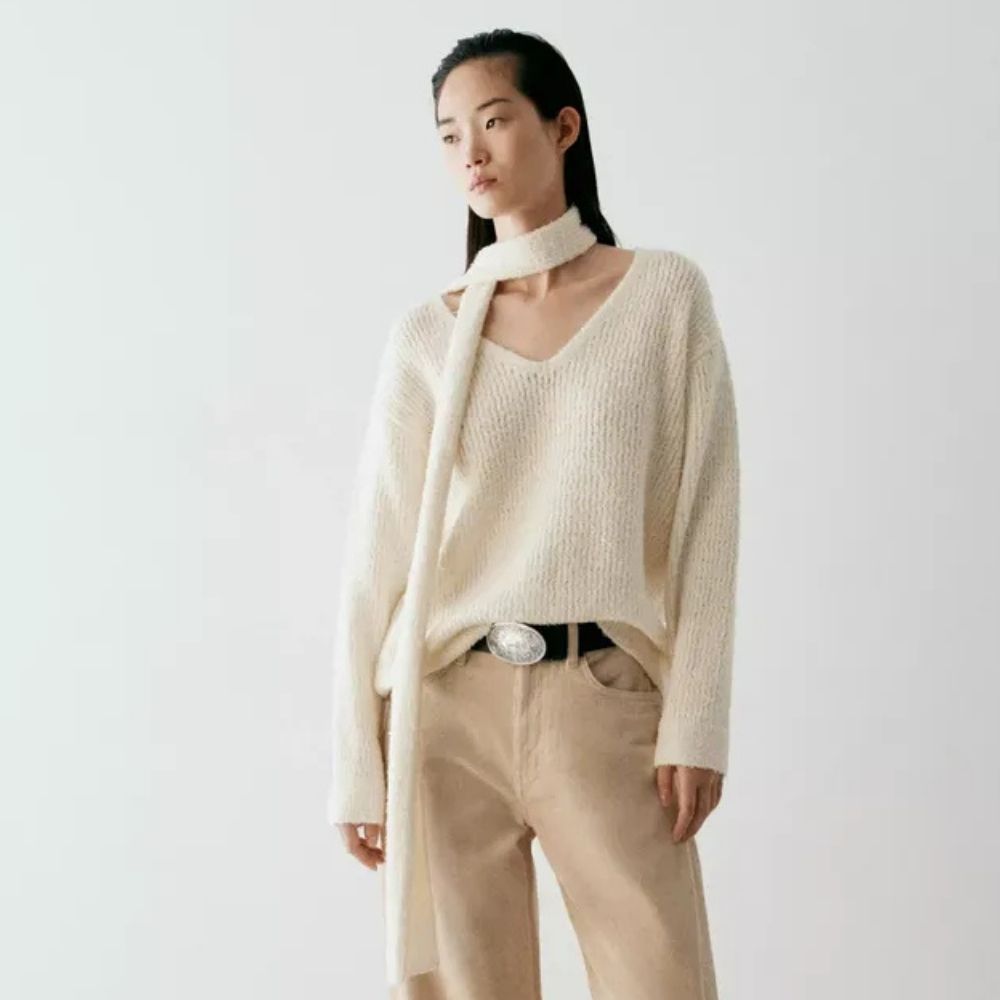 Woman wears cream coat with high collar, black trousers