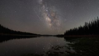 The Milky Way is reflected in an Alpine Lake as three Leonid meteors streak overhead.