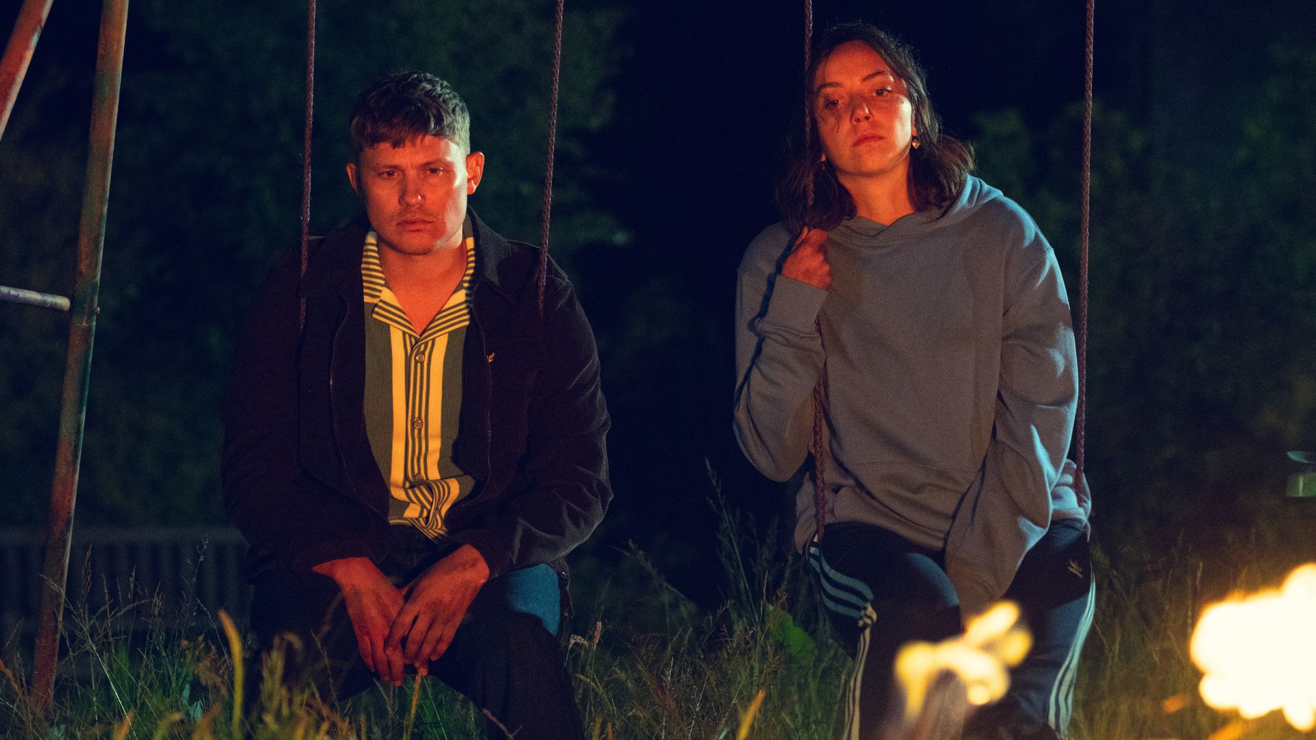 Ash and Dee Dee sit on swings watching a fire burn
