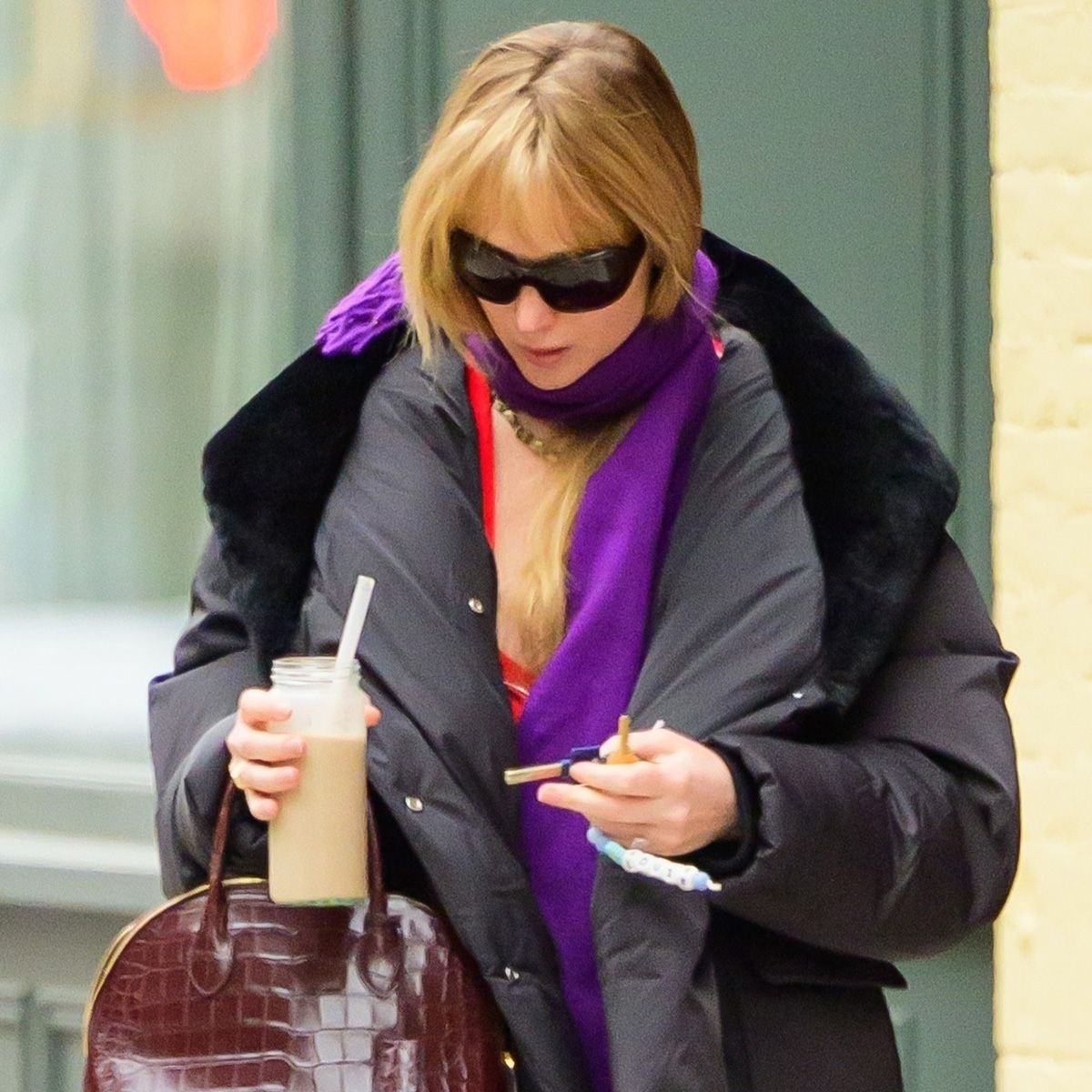 Jennifer lawrence wears black sunglasses, a purple scarf, black puffer jacket, and a brown croc bag.