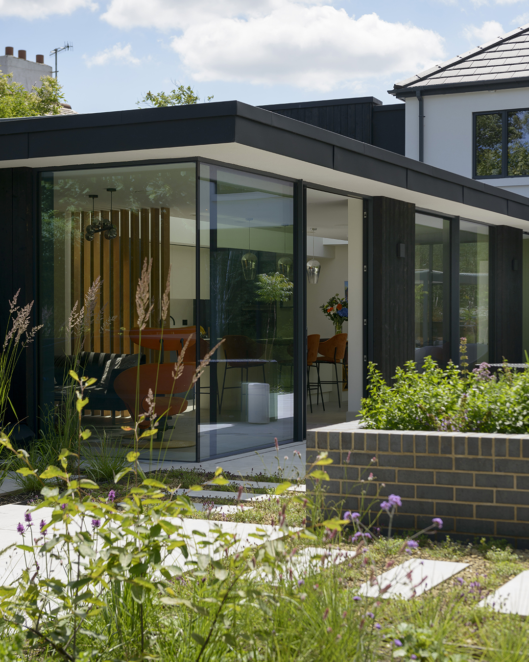 A glazed extension with black cladding with newly landscaped garden with paving and planting