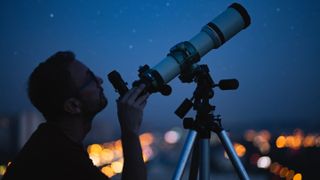 Best telescopes under $500: Image shows man using telescope at night with blurred city lights in background