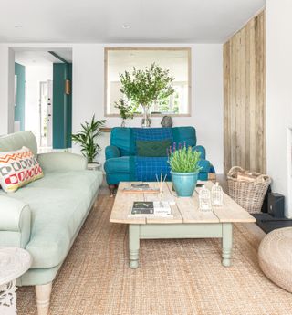 living room with pale green and teal sofas with wooden coffee table and rattan pouffe