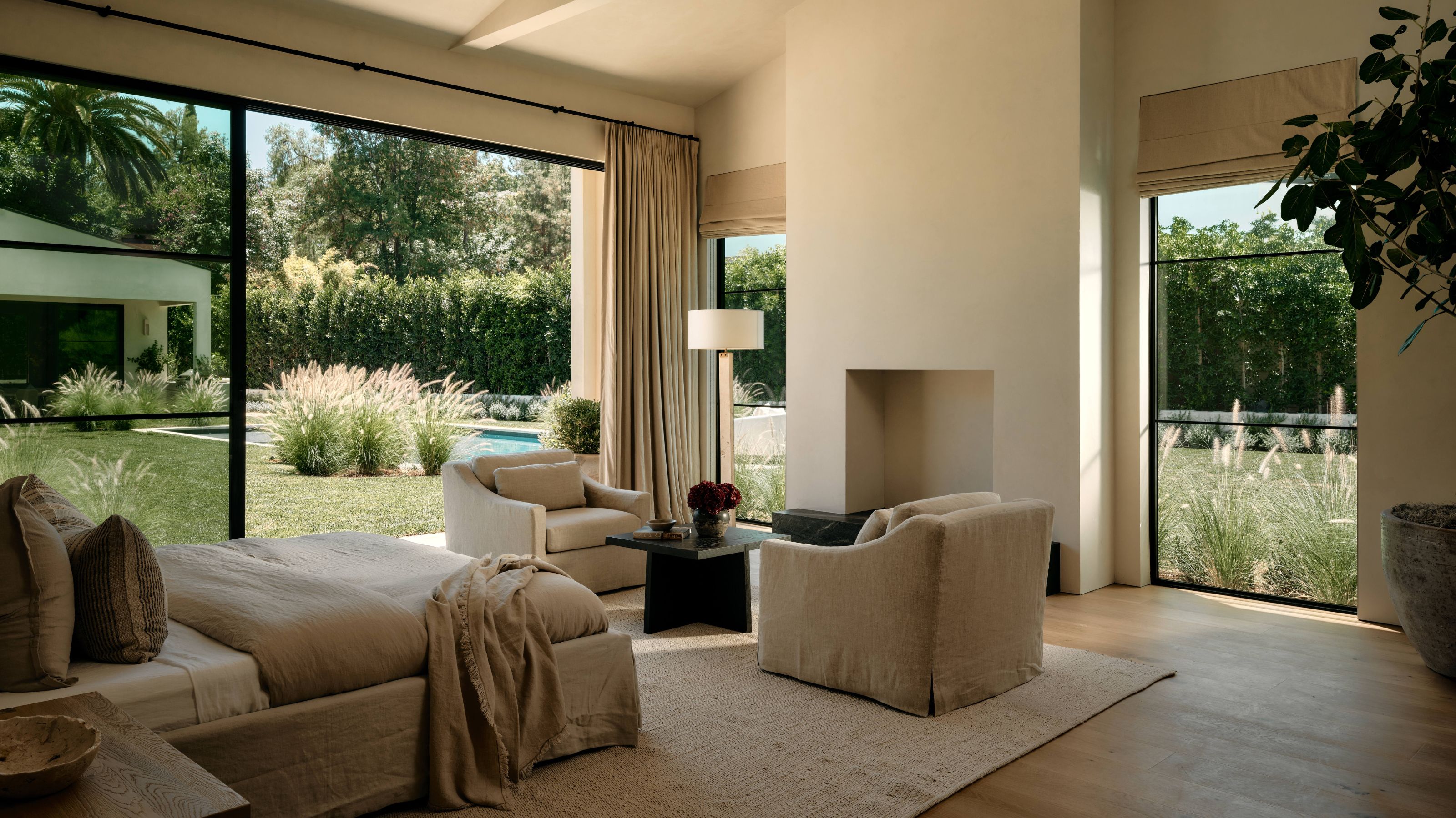 a large airy neutral primary bedroom with glass patio doors and a large plaster fireplace