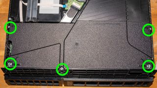 A photo of the PS4 power supply with the screws that need removing highlighted in green circles