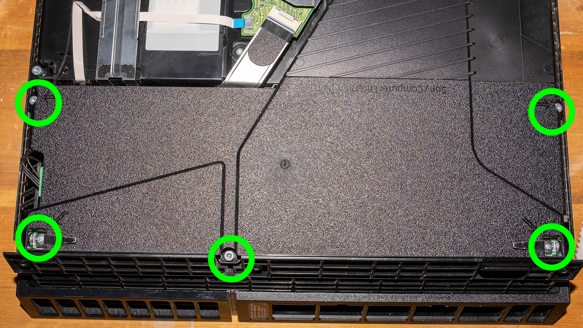 Фотография блока питания PS4 с винтами, которые необходимо открутить, выделенными зелеными кружками.