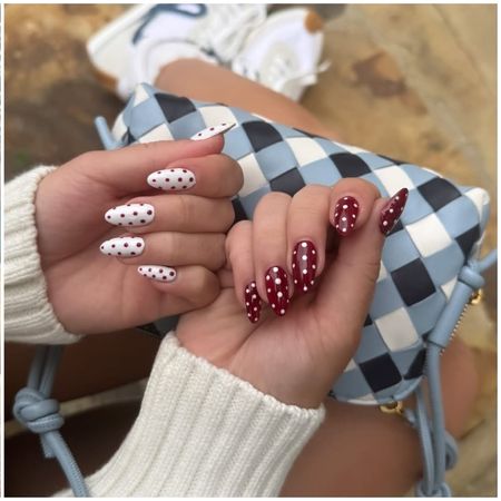 red and white polka dot nails shot close up on a woman's hands over a checkered purse and white sweater sleeves