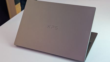 A sleek XPS 13 laptop displaying a tech news website on a light-colored table.