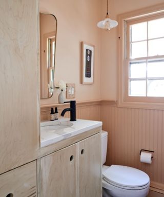 small powder room with peach walls, light wooden vanity, white fixtures