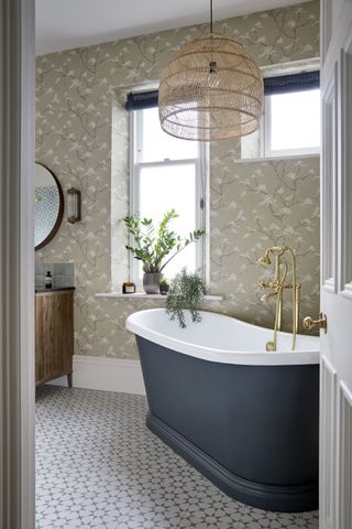 bathroom ceiling lighting ideas with rattan pendant, floral wallpaper, patterned tiled floor and blue bath by BC Designs