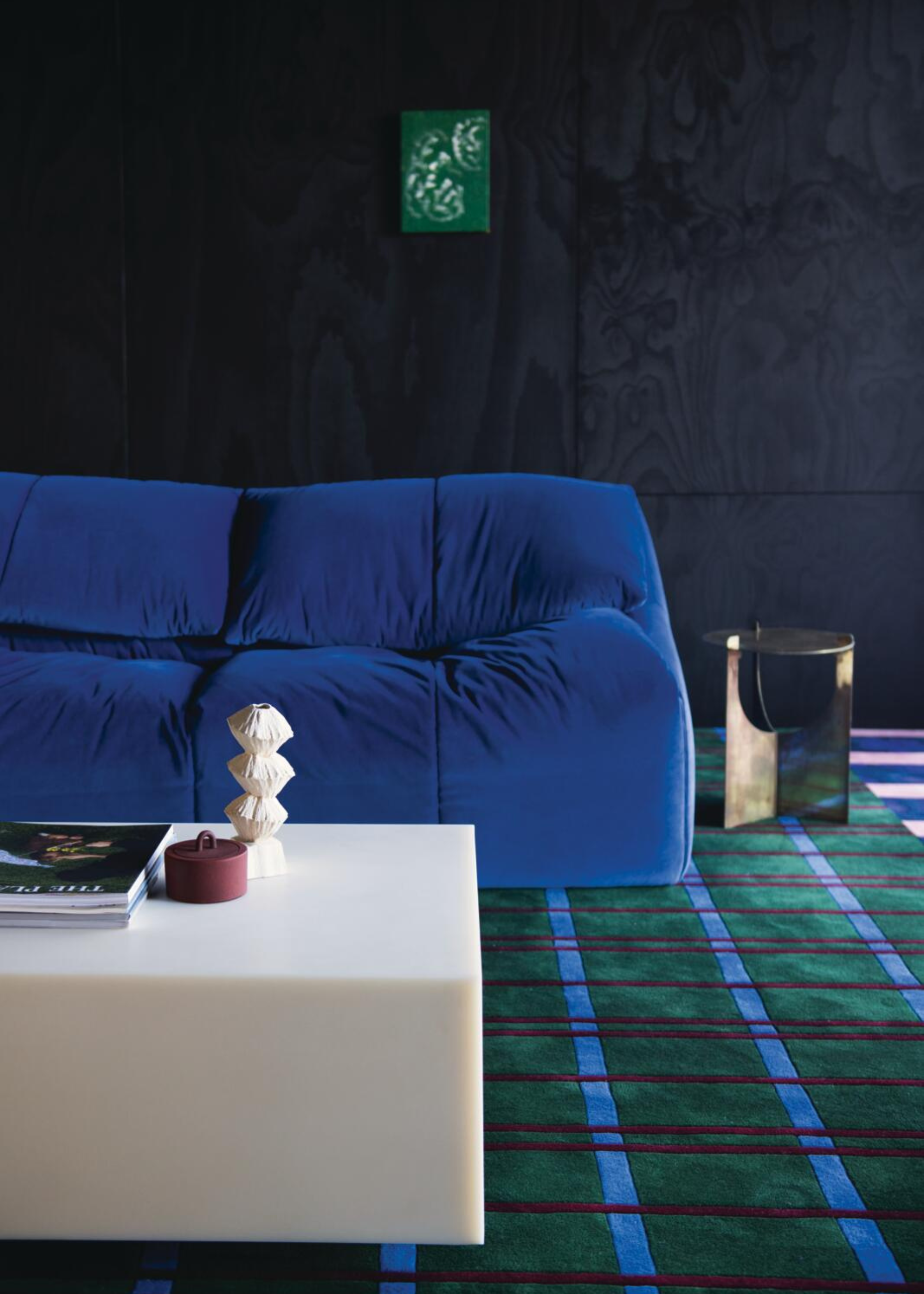 a blue sofa in a living room with colorful patterned green and blue rug and a square stone coffee table and dark wall paint behind