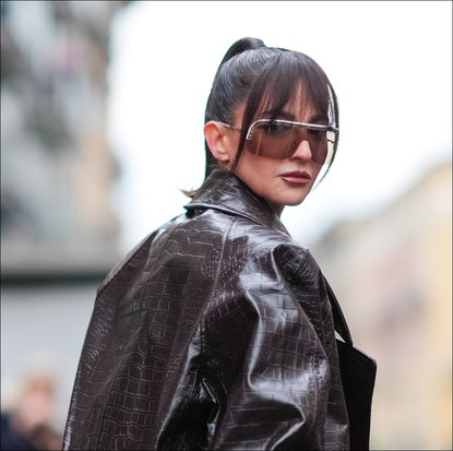 Alexandra Pereira wears sunglasses, a brown oversized leather jacket with crocodile patterns, a colored top with printed geometric patterns, brown underwear, brown tights, outside Missoni, during the Milan Fashion Week - Womenswear Fall/Winter 2024-2025 on February 24, 2024 in Milan, Italy.
