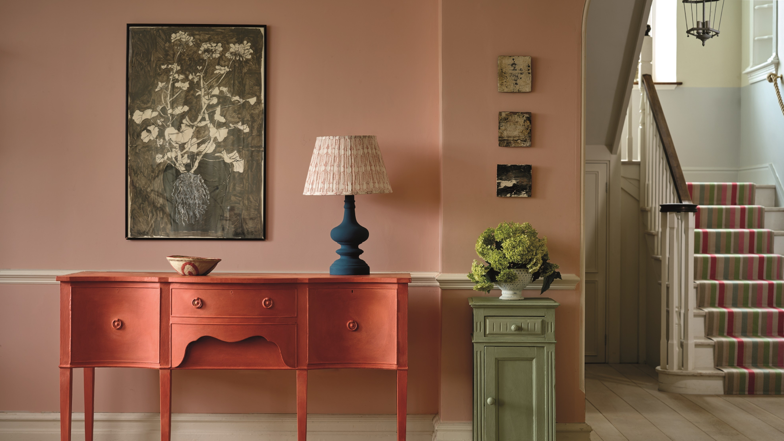 hallway painted in soft terracotta with painted sideboard, table, blue table lamp with patterned shade and lantern pendant light showing in stairwell as hallway lighting ideas