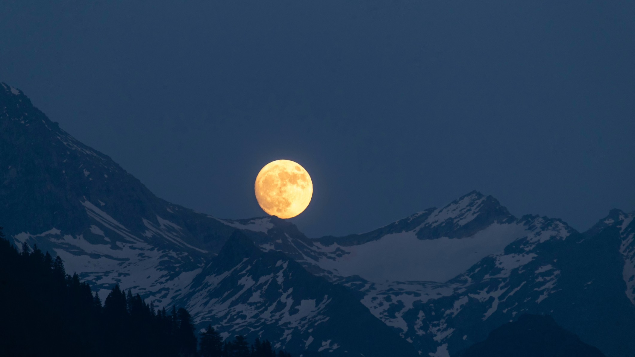 A brilhante lua cheia surge sobre as montanhas cobertas de neve.
