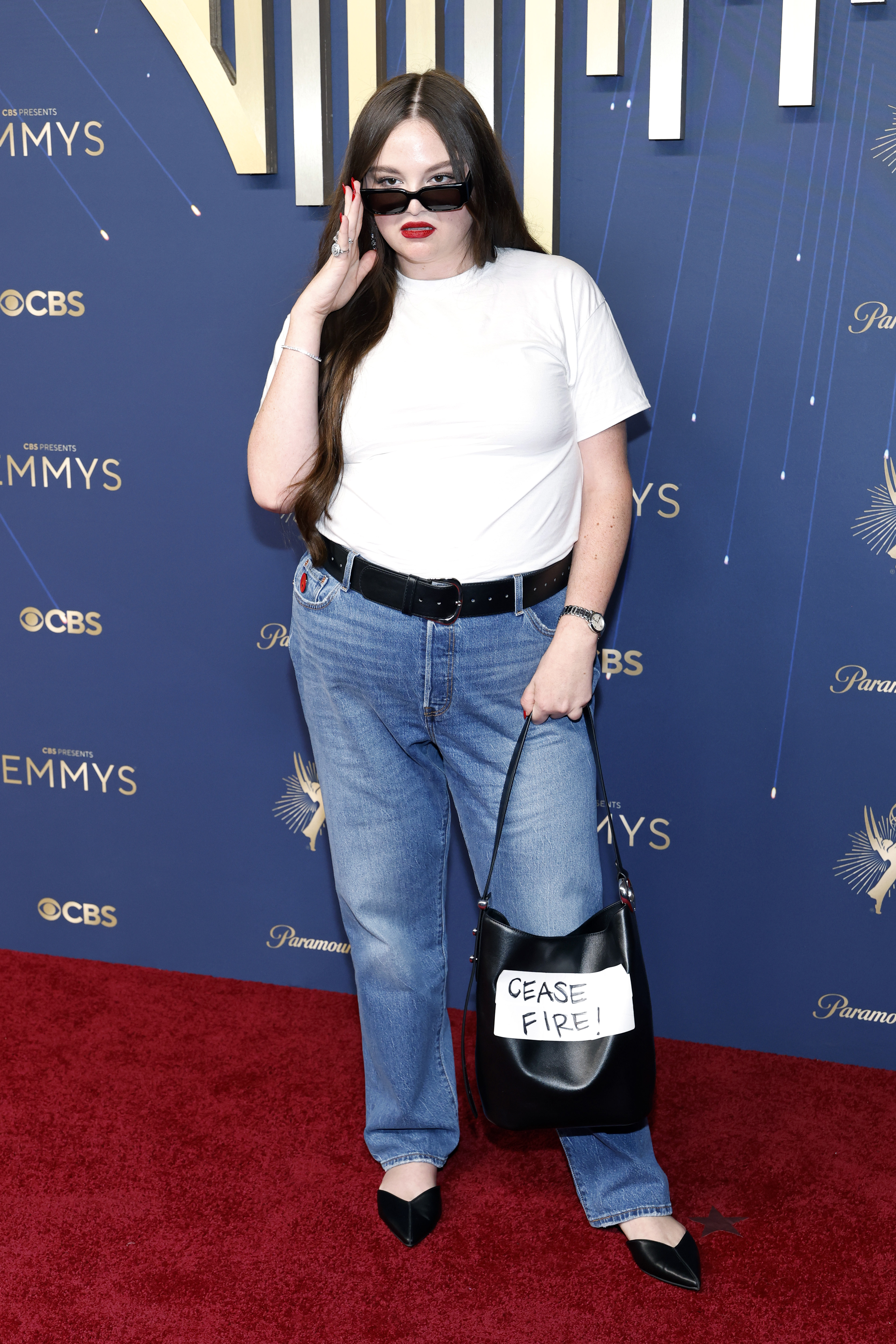 Meg Stalter attends the 2025 emmy awards in jeans a tshirt and a cease fire bucket bag