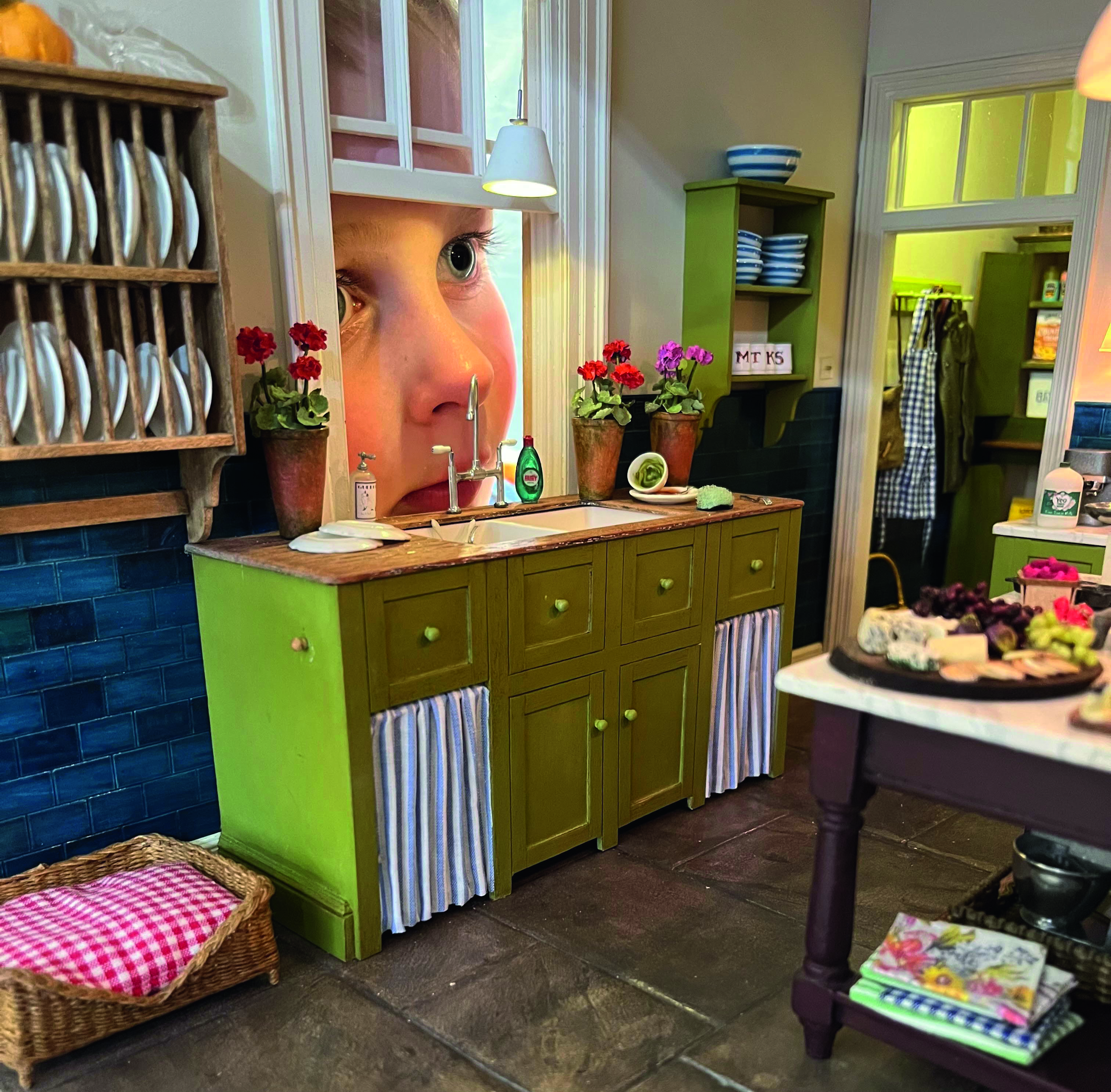 A boy peers through a window into a dollshouse kitchen. The boy is giant in comparison