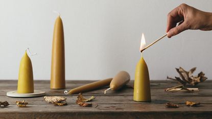 A hand holding a long match to light one of a group of yellow beeswax candles