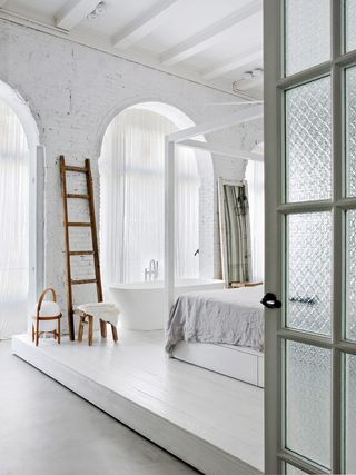 rustic bedroom with freestanding bath and large arched windows with sheer drapes