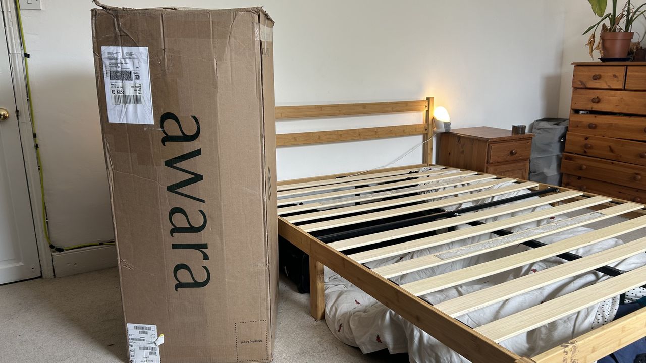 The Awara Classic Hybrid in a cardboard box next to a wooden bedframe