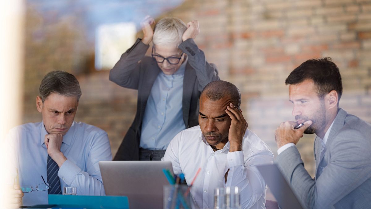 A frustrated IT team suffering from burnout, viewed from behind glass.