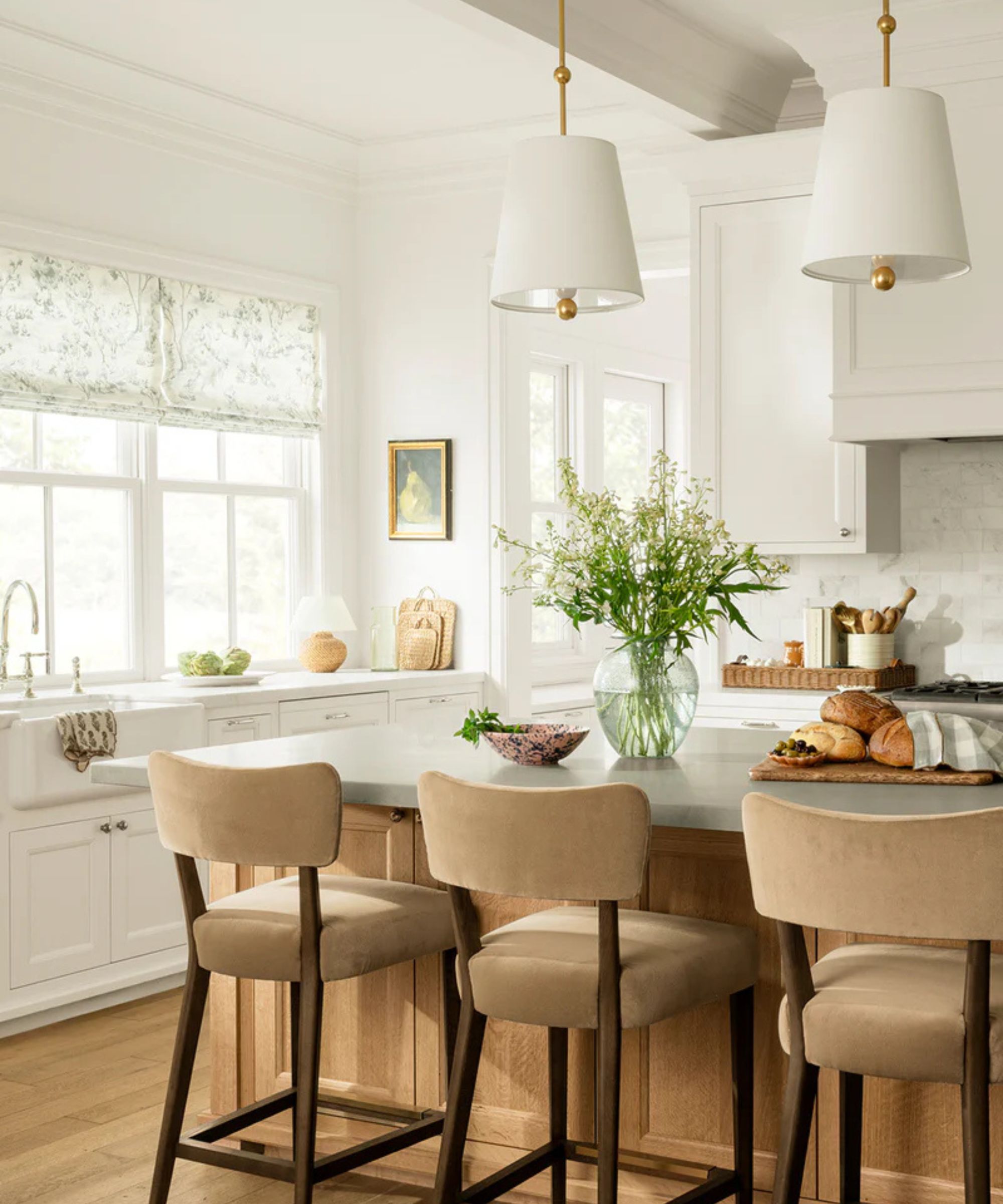 A white kitchen with a light wood island, brass hardware, and white pendant lights
