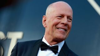 Bruce Willis wears a tuxedo and bow tie in front of a blue background. He was attending the Comedy Central Roast of Bruce Willis at Hollywood Palladium on July 14, 2018 in Los Angeles, California.
