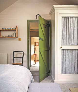 bedroom with patterned wallpaper, green door, white cupboard with door curtain
