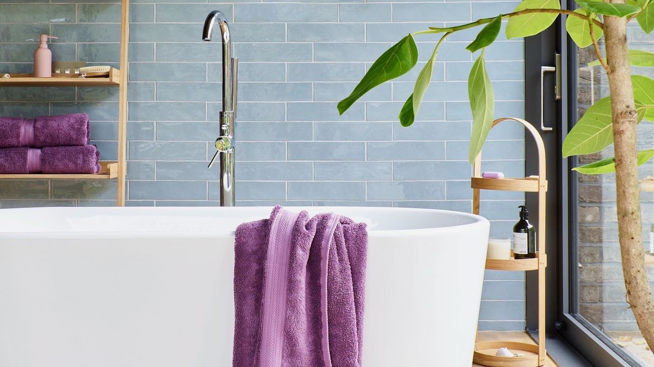 Purple towels and while bath with powder blue tiles