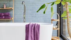 Purple towels and while bath with powder blue tiles
