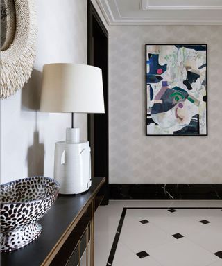 Entryway with bold artwork, table lamp, console and stone floor