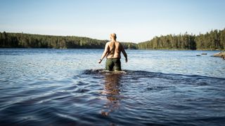 Man enters cold body of water in his swimming trunks