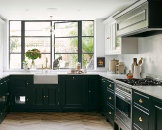 a mid-century black kitchen with dark cupboard doors, with a white sink and gold tap, white countertops and a big, black window